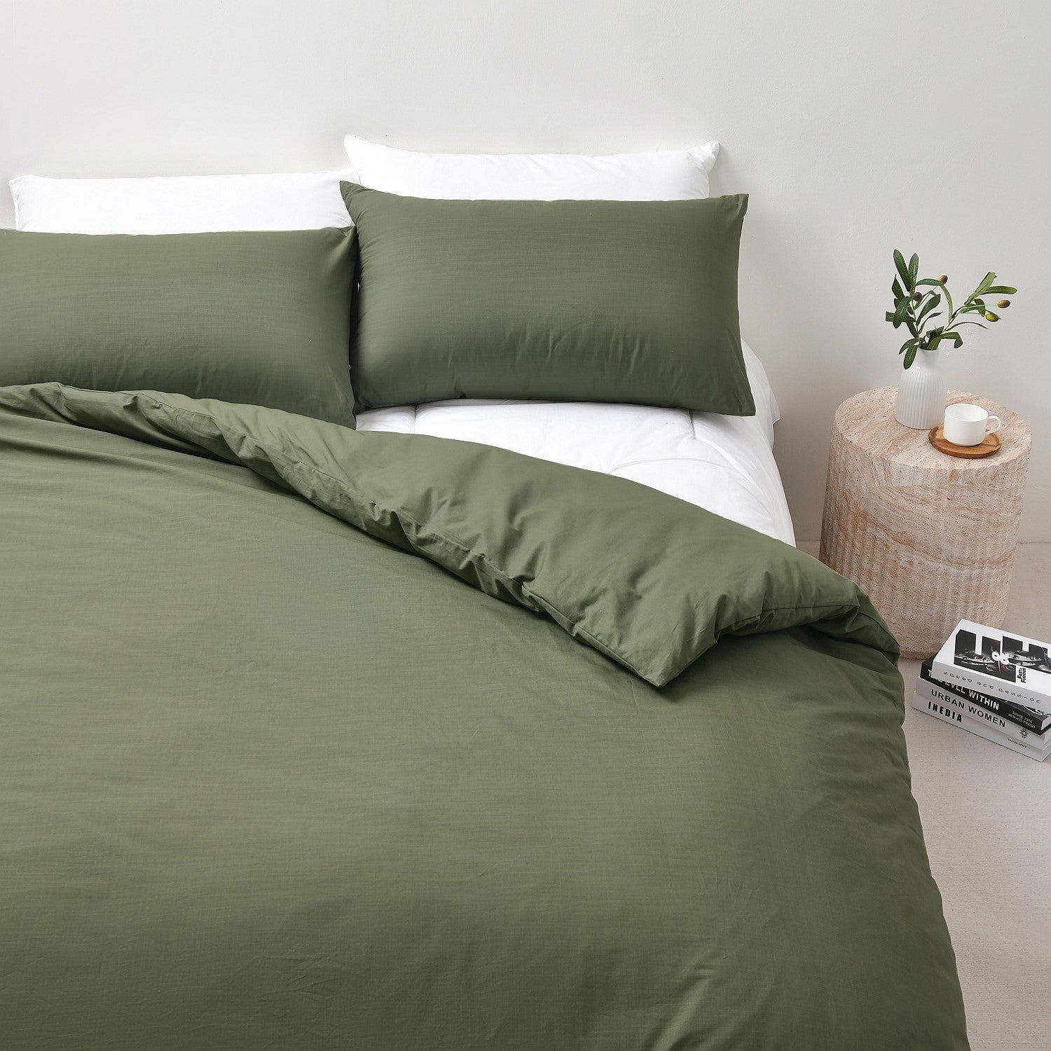 Green bedding set on a bed with a side table and plant in the background