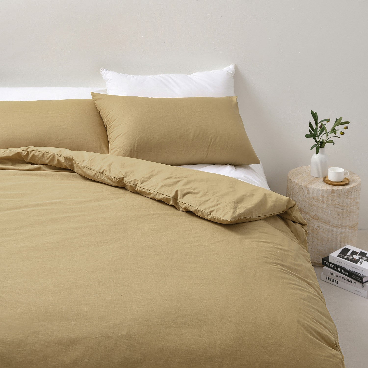 Beige bedding set on a bed with a white pillow and side table with a plant.