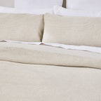 Beige textured bedspread and pillows on a bed with white bedding.