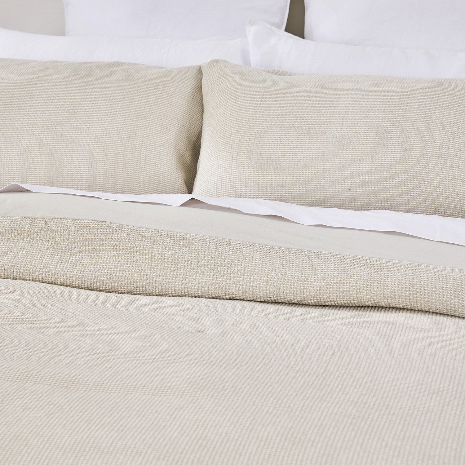 Beige textured bedspread and pillows on a bed with white bedding.