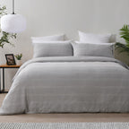 Gray striped duvet cover set on a bed in a bedroom with plants and a lamp.