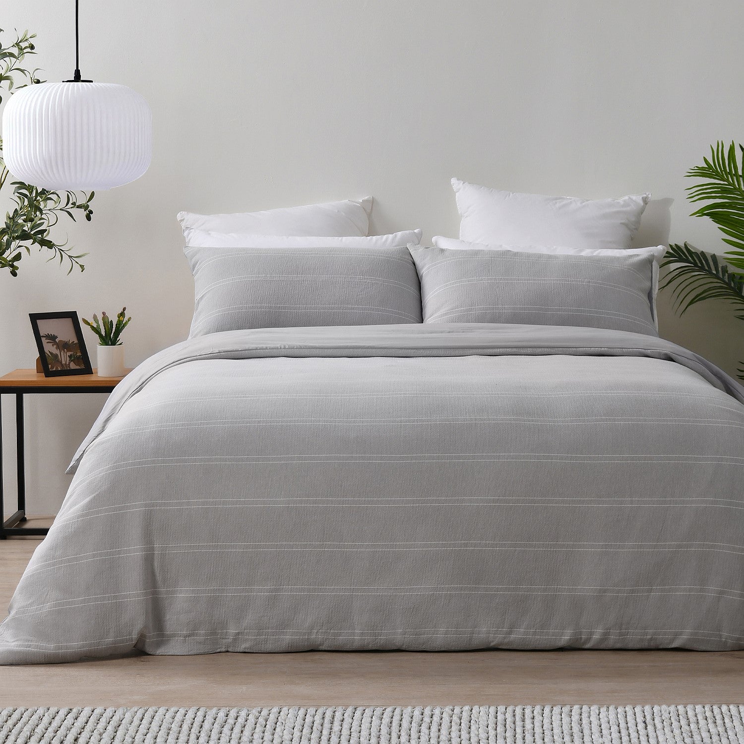 Gray striped duvet cover set on a bed in a bedroom with plants and a lamp.