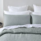 Gray bedding set with white pillows on a bed against a gray wall.