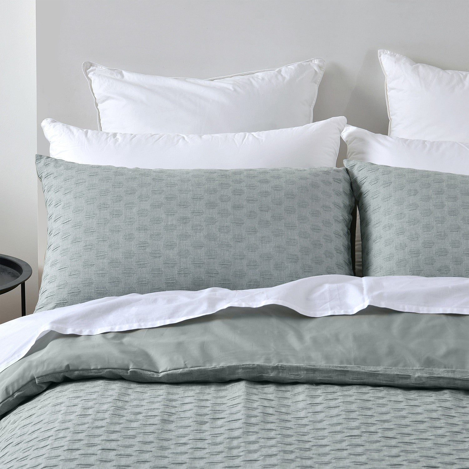 Gray bedding set with white pillows on a bed against a gray wall.