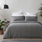 Gray checkered duvet set on a bed in a room with plants and a lamp.