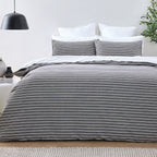 Bed with gray striped bedding in a minimalistic bedroom setting.