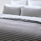Gray and white striped bedding set with pillows on a bed.