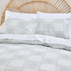 Bed with gray checkered duvet and white pillows against a wooden headboard.