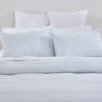 Light blue striped bedding set with white pillows on a neutral background