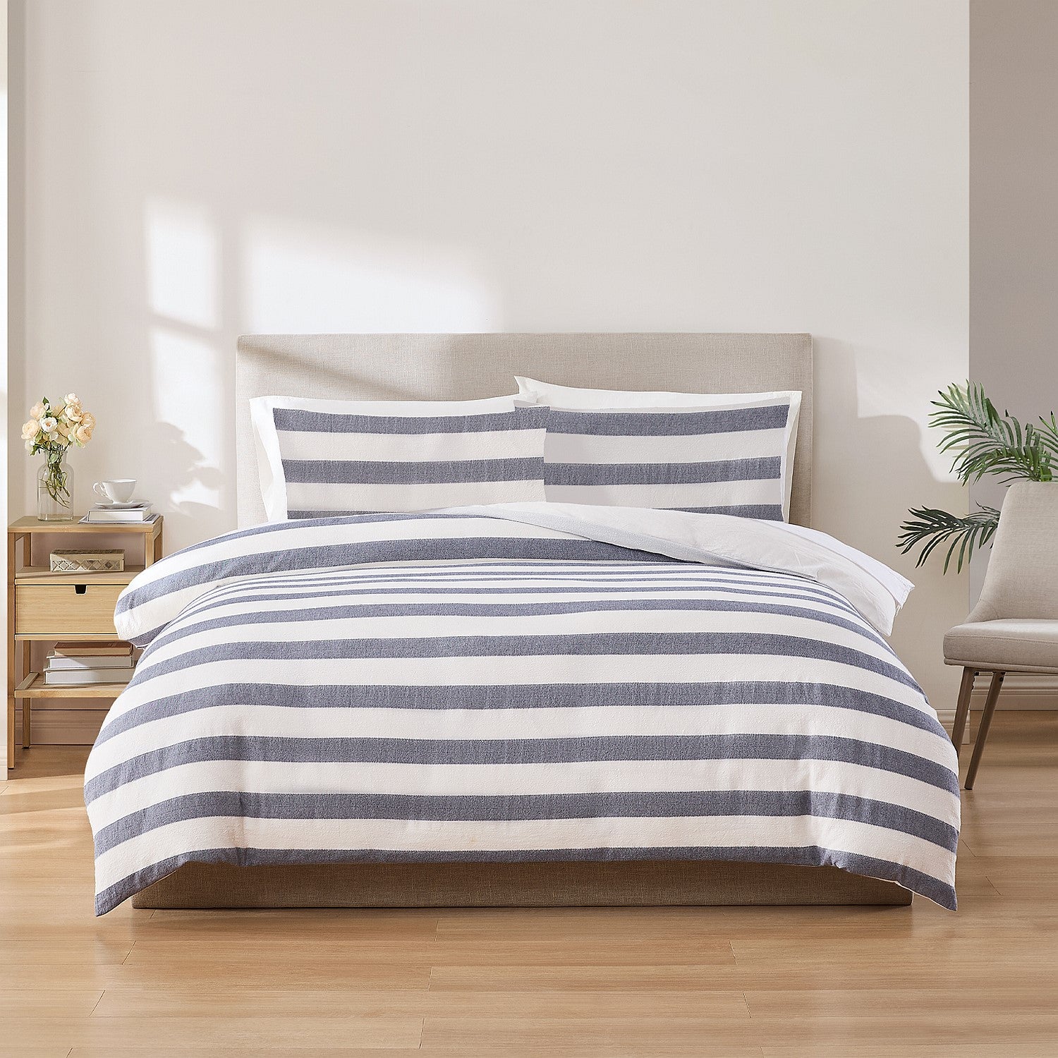 Striped bedding set on a bed in a bedroom with a nightstand and chair.