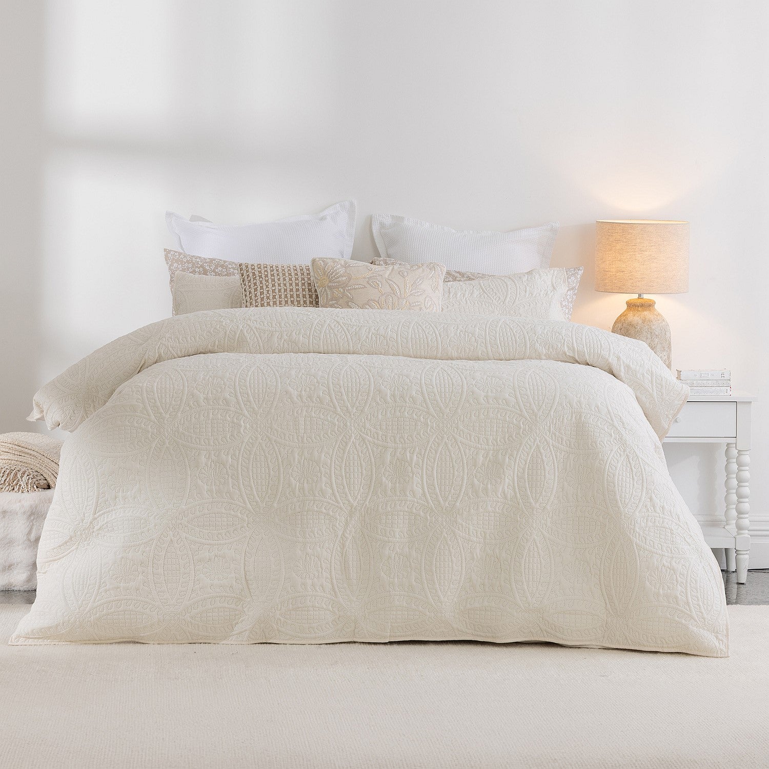 Neatly made bed with beige textured duvet and pillows in a bright bedroom.