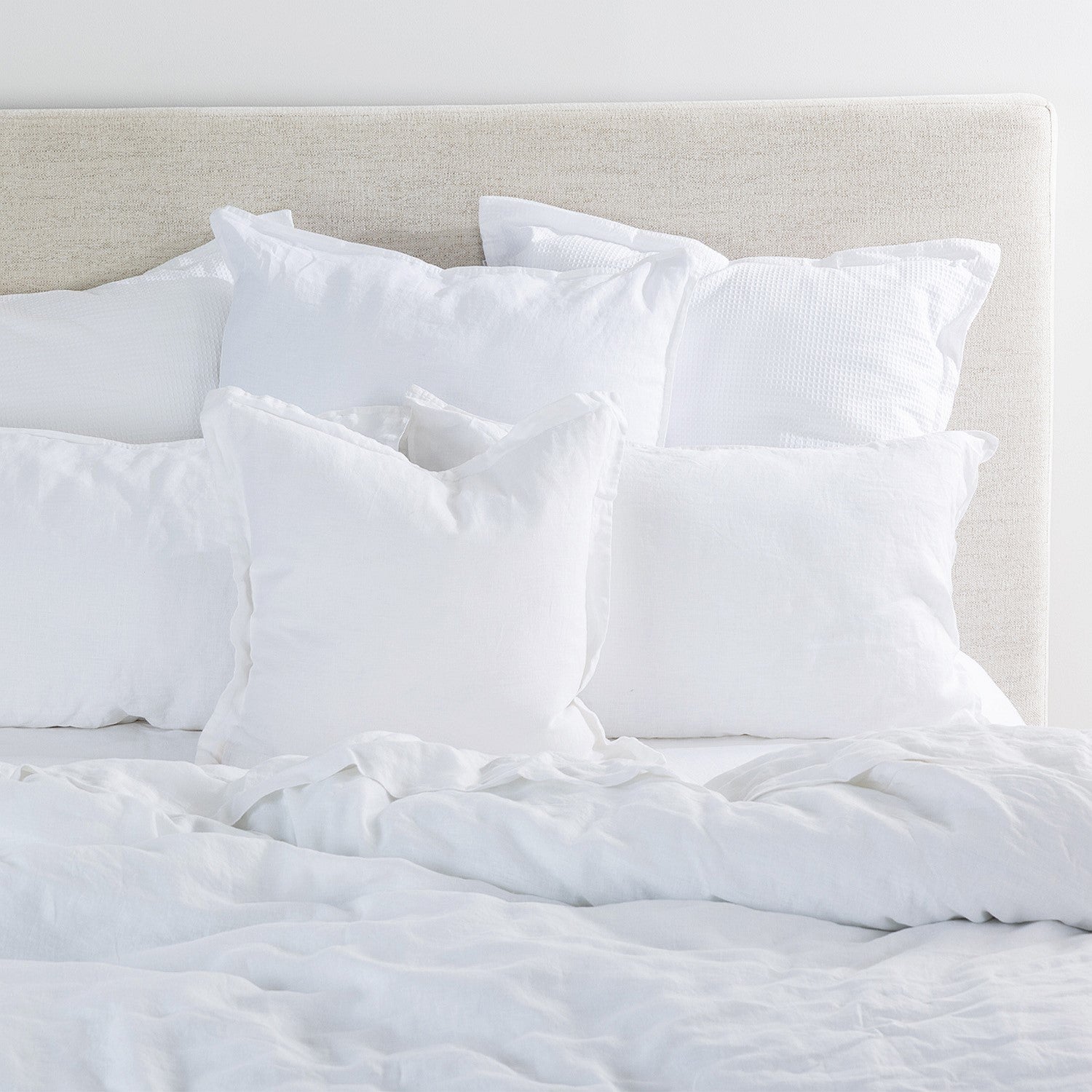 White pillows and comforter on a bed with a neutral headboard.