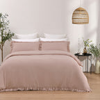 Bed with pink bedding and white pillows in a room with a wicker lamp and plants.