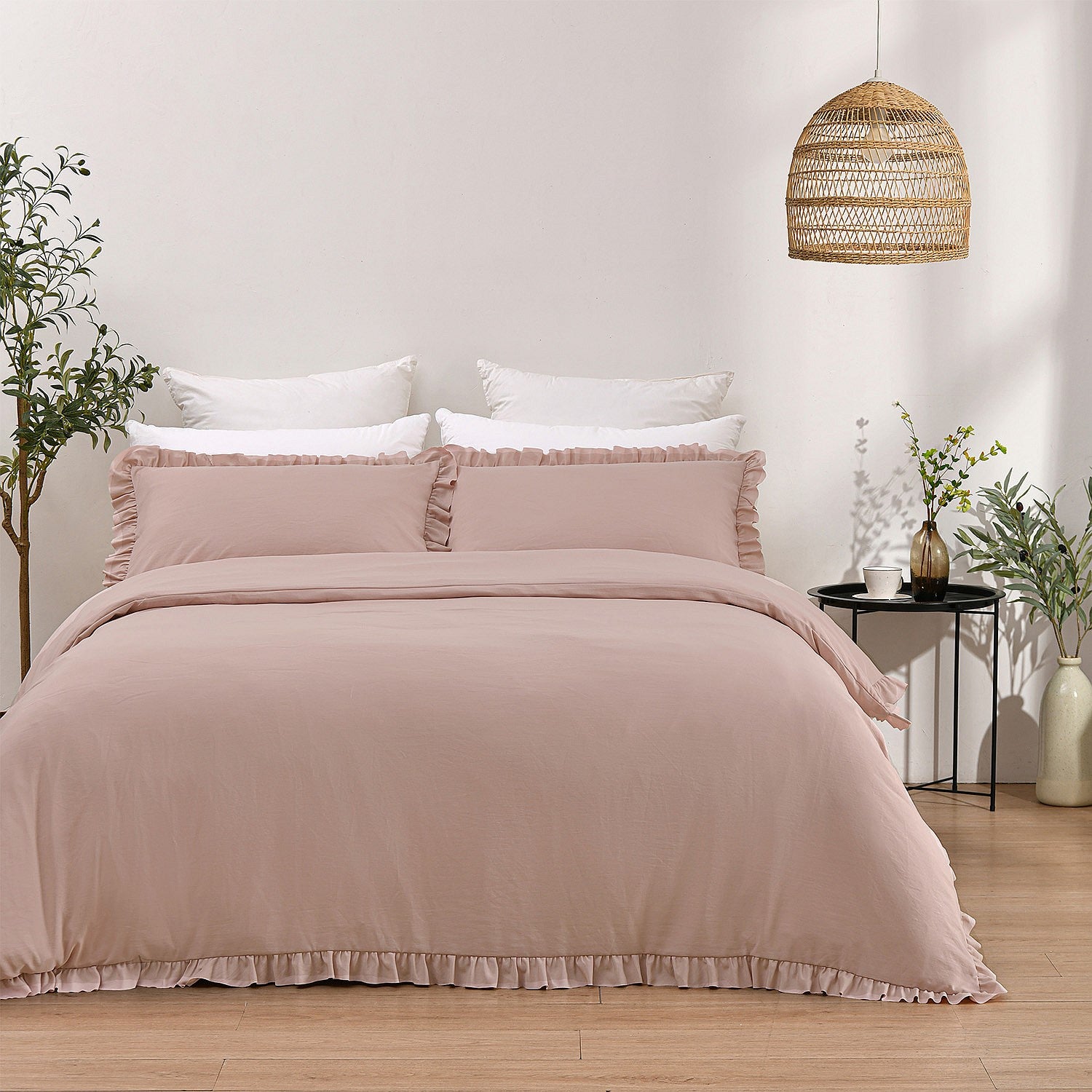 Bed with pink bedding and white pillows in a room with a wicker lamp and plants.