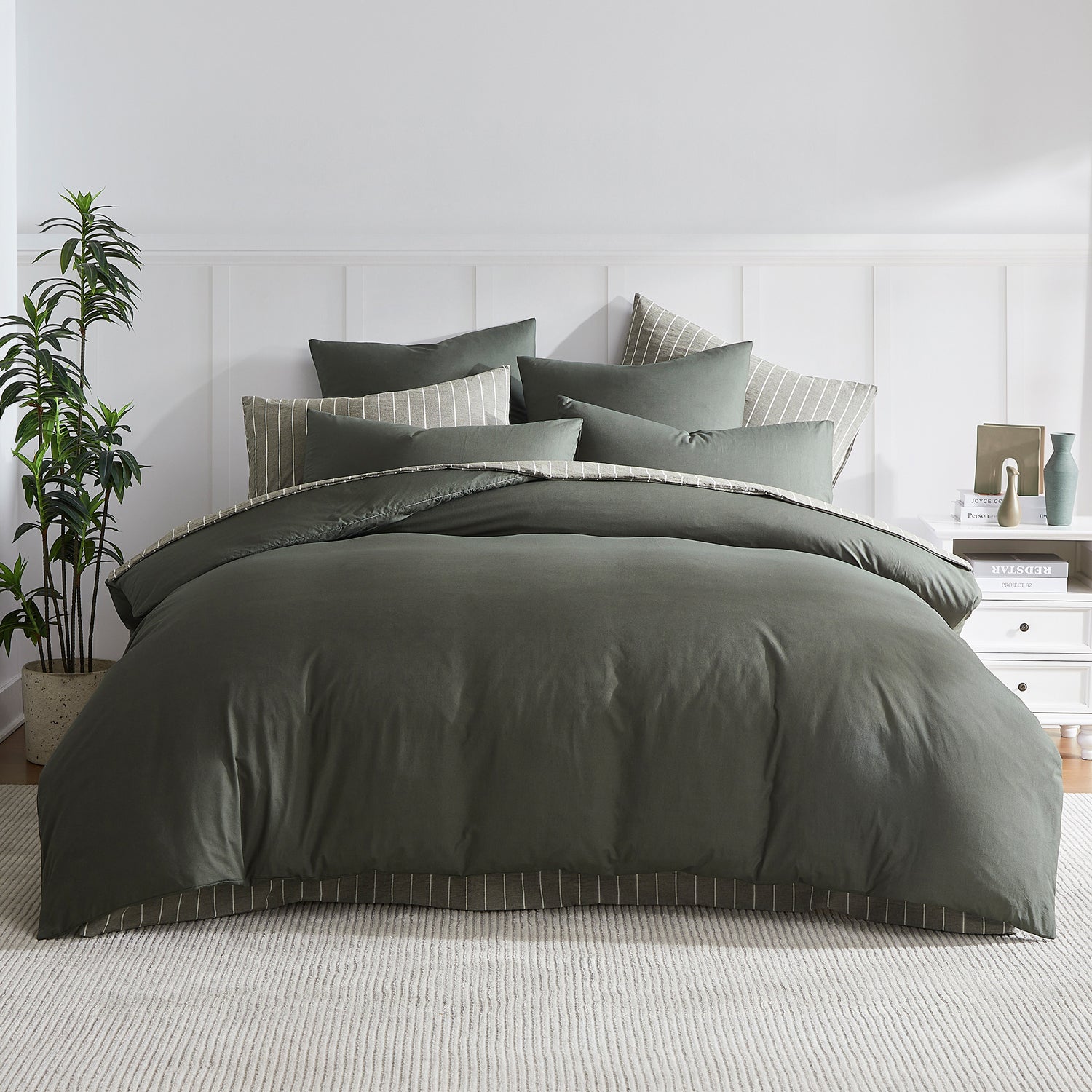 A beautifully styled bed dressed in rich thyme green bedding is layered with coordinating pinstripe cushions for a relaxed, contemporary bedroom look.