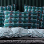 A styled bedding set featuring patterned pillows and a striped duvet cover on a bed against a dark paneled wall.