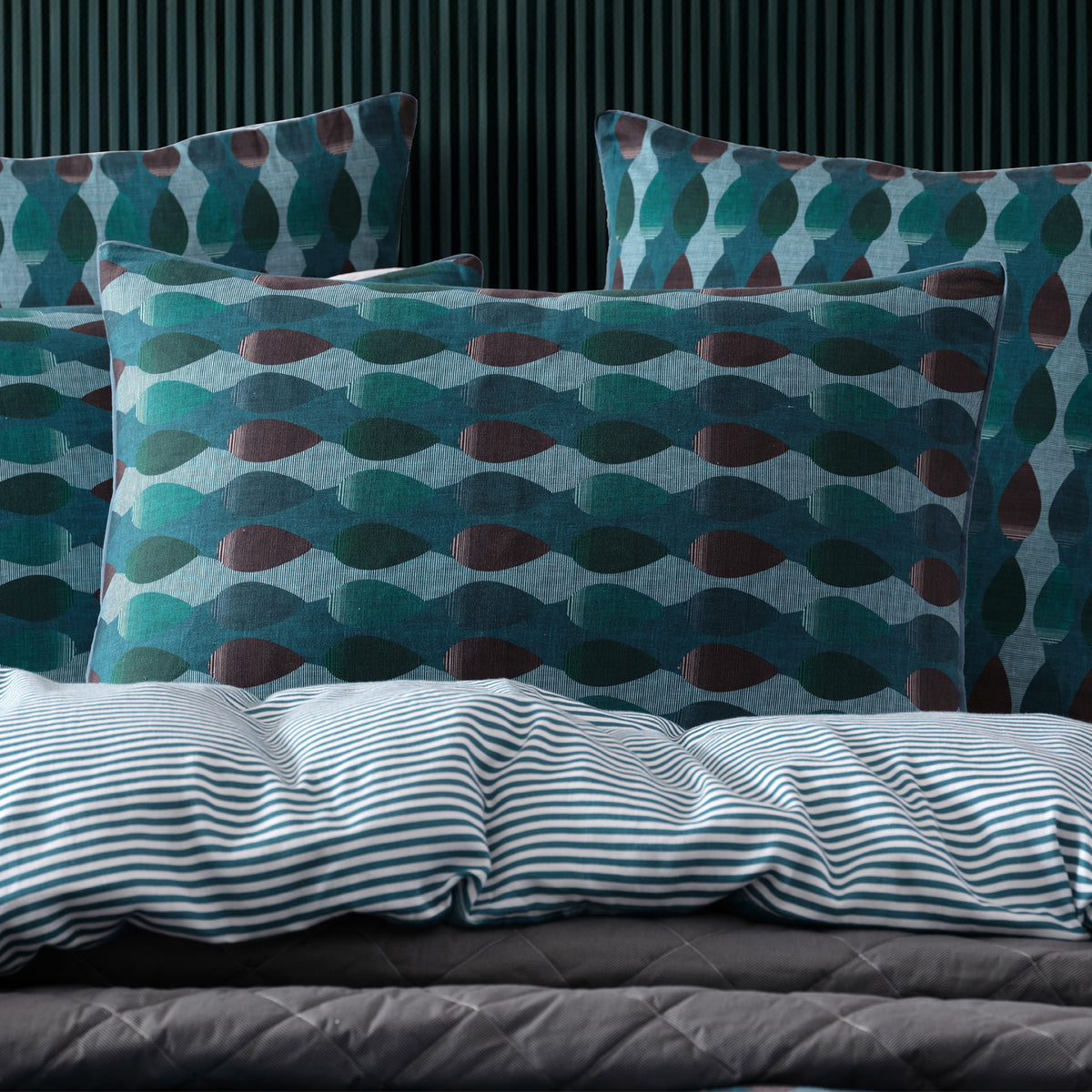 A styled bedding set featuring patterned pillows and a striped duvet cover on a bed against a dark paneled wall.