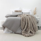 Grey lyocell and cotton duvet cover set styled on a bed with layered white pillows and a taupe faux fur throw in a soft, contemporary bedroom setting.