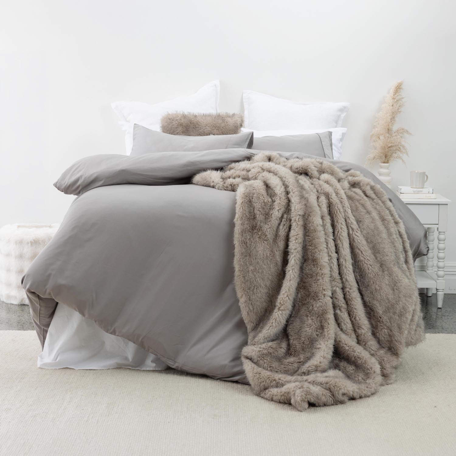 Grey lyocell and cotton duvet cover set styled on a bed with layered white pillows and a taupe faux fur throw in a soft, contemporary bedroom setting.