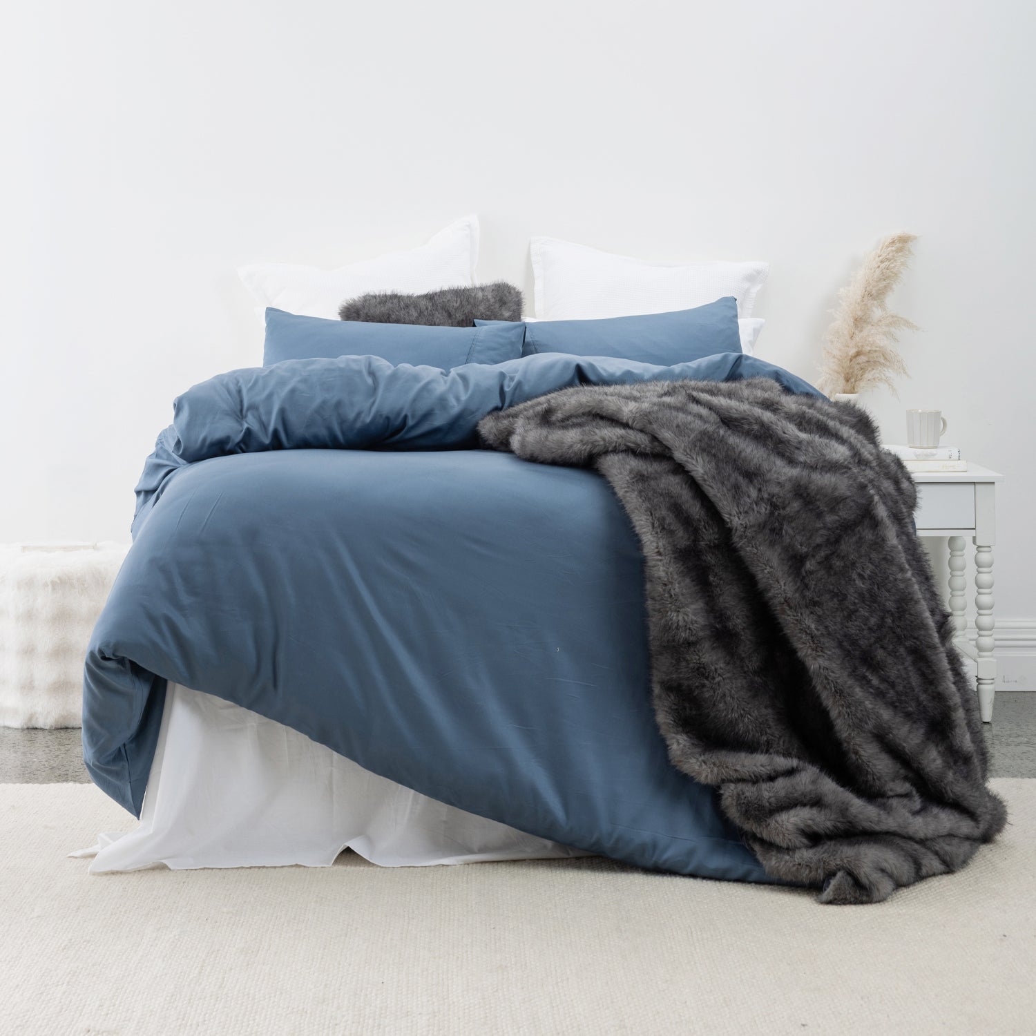 Navy blue lyocell and cotton duvet cover set styled with white pillows and a charcoal faux fur throw in a modern, minimalist bedroom.