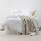 White lyocell and cotton duvet cover set styled with layered white bedding and a soft neutral throw in a bright, minimalist bedroom setting.