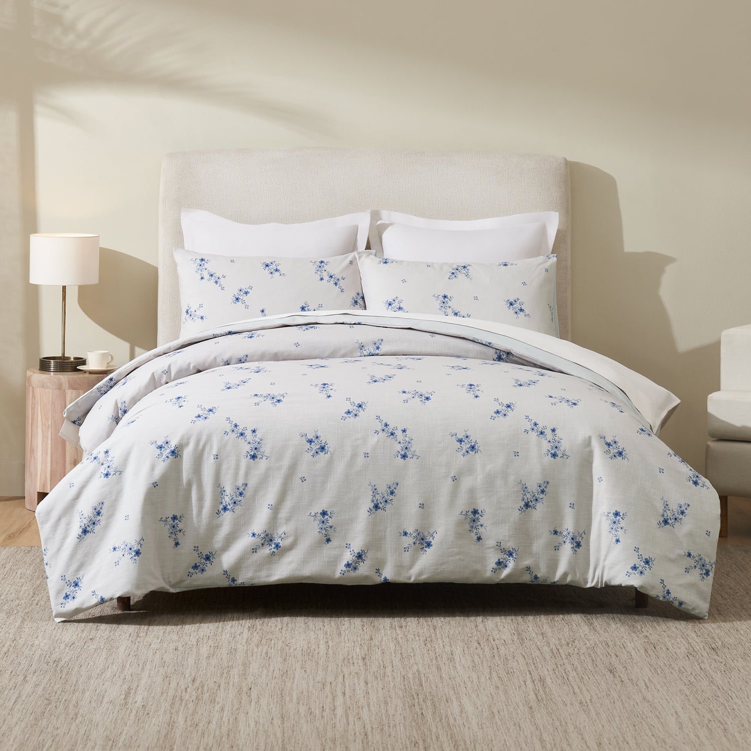 A beautifully styled bed dressed in soft white bedding with delicate blue floral sprigs creates a fresh, airy bedroom with timeless cottage-inspired charm.