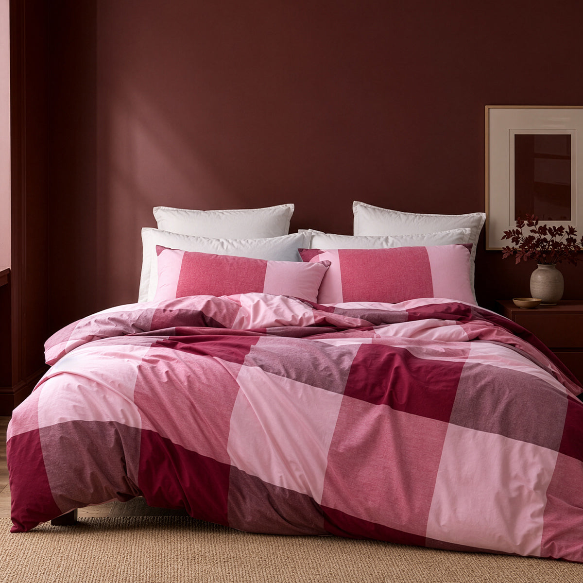 Bed with pink and red checkered duvet and pillows against a dark brown wall.
