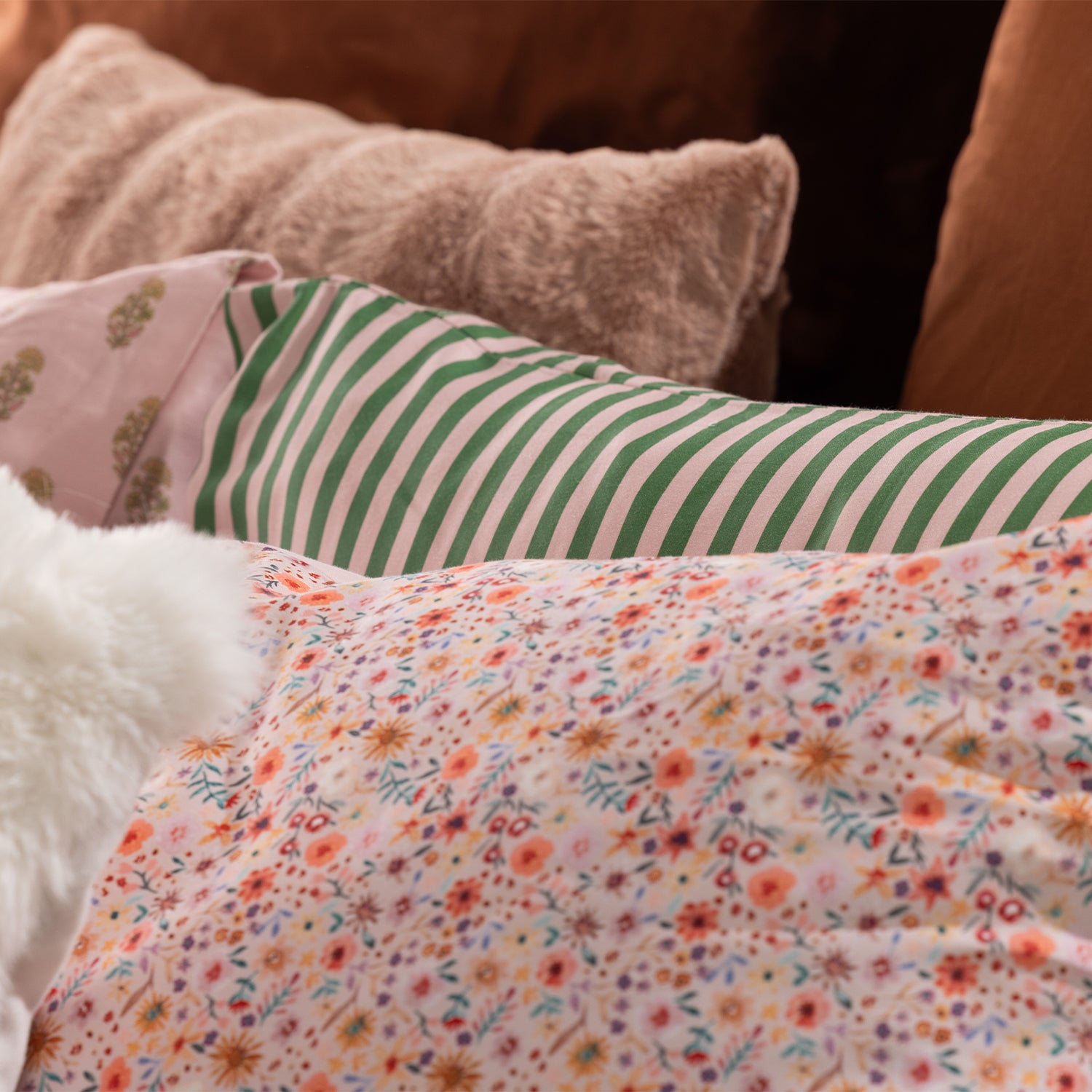 Close-up of Marlo Mia Floral bedding styled with floral print, green and pink striped pillowcase, and textured accent cushions.