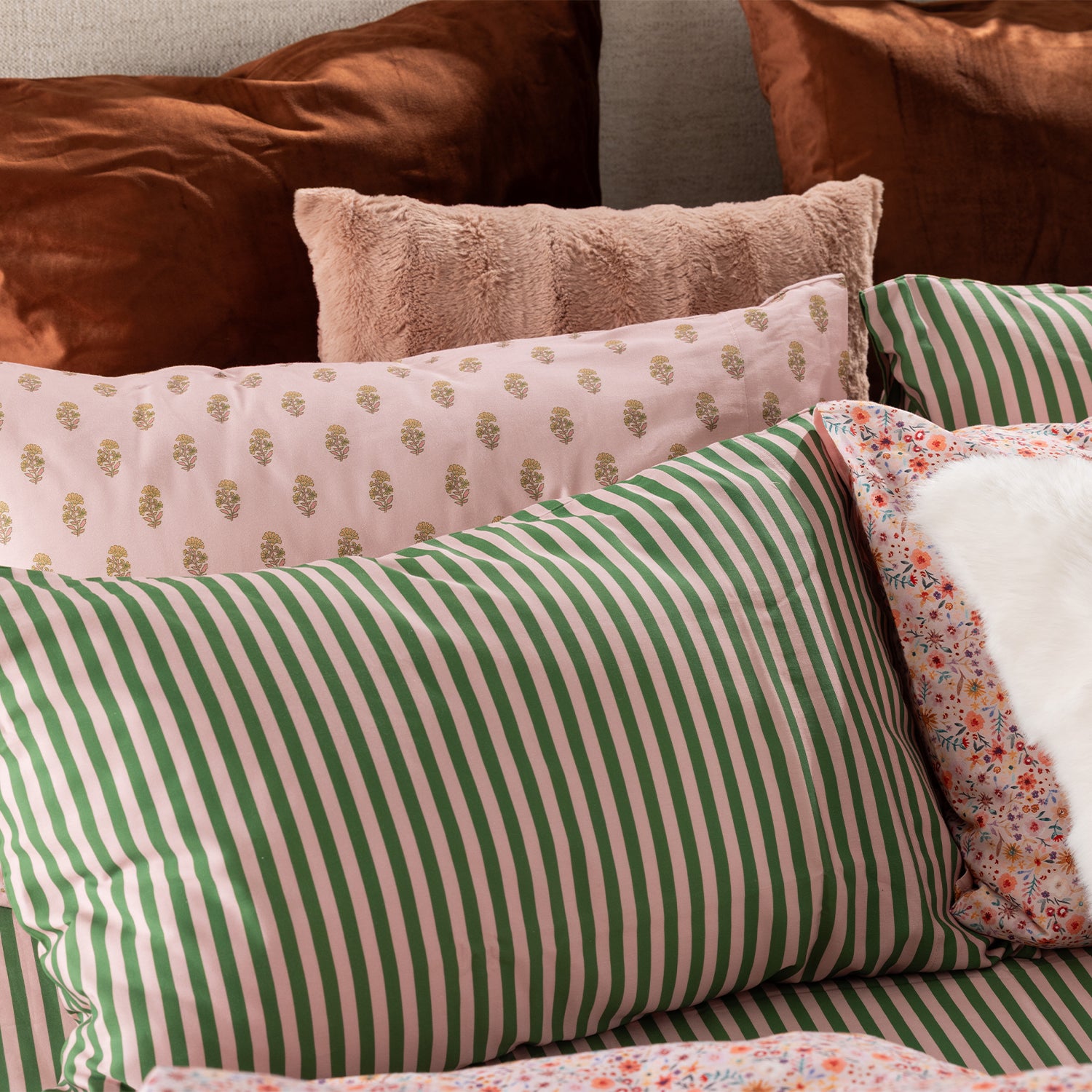 Close-up of Marlo Mia Stripe pillowcases styled with coordinating blush and rust-toned cushions.