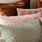Close-up of Marlo Mia bedding styled with blush botanical print pillowcases, green striped pillowcases, and textured accent cushions.