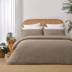 Fieldcrest Maison cotton duvet cover set in mocha with a textured geometric pattern styled on a bed with a rattan headboard and timber bedside table.