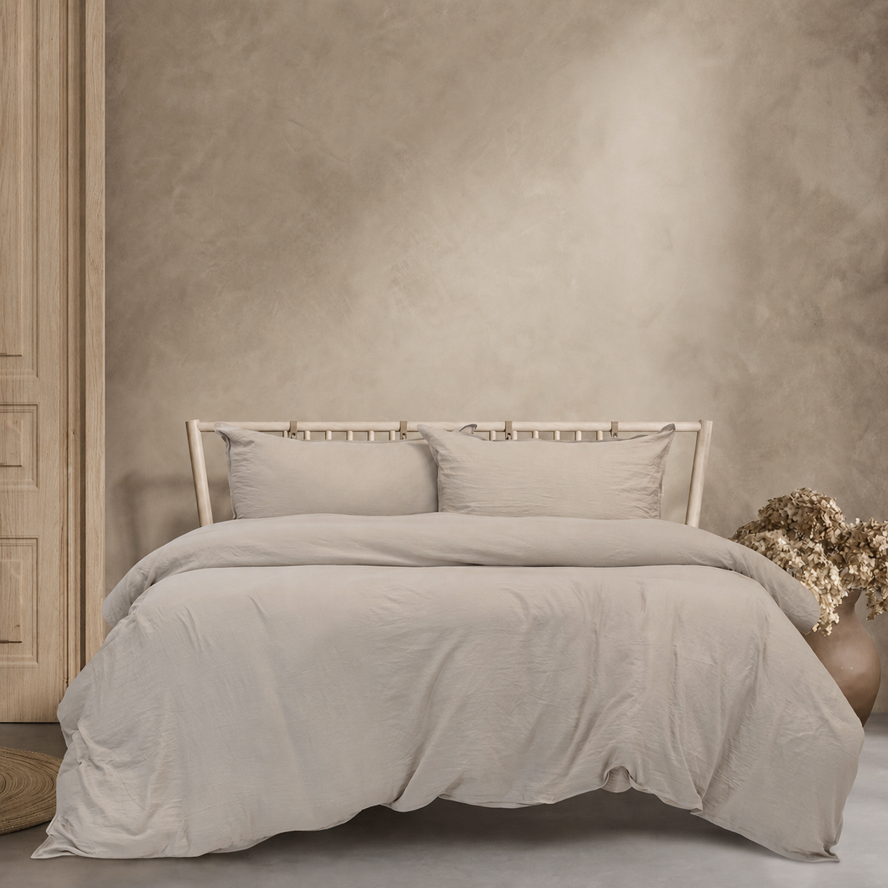 Beige bedding set on a bed against a beige wall with a vase of flowers.