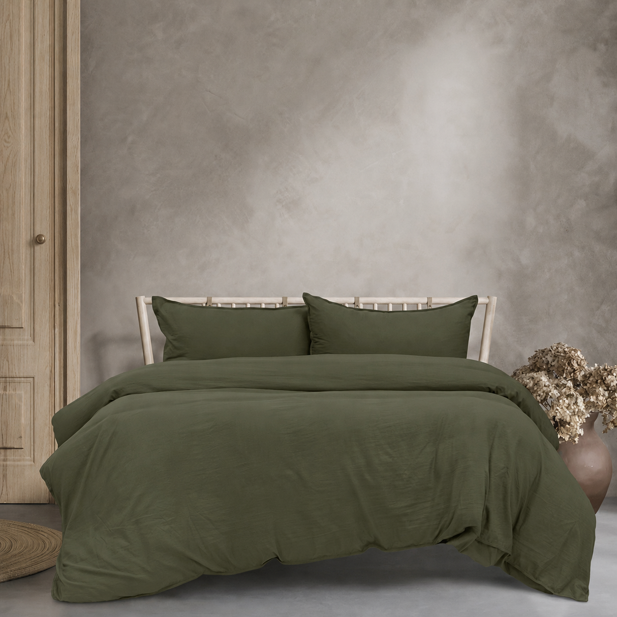 Green bedding set on a bed against a gray wall with a vase of flowers.