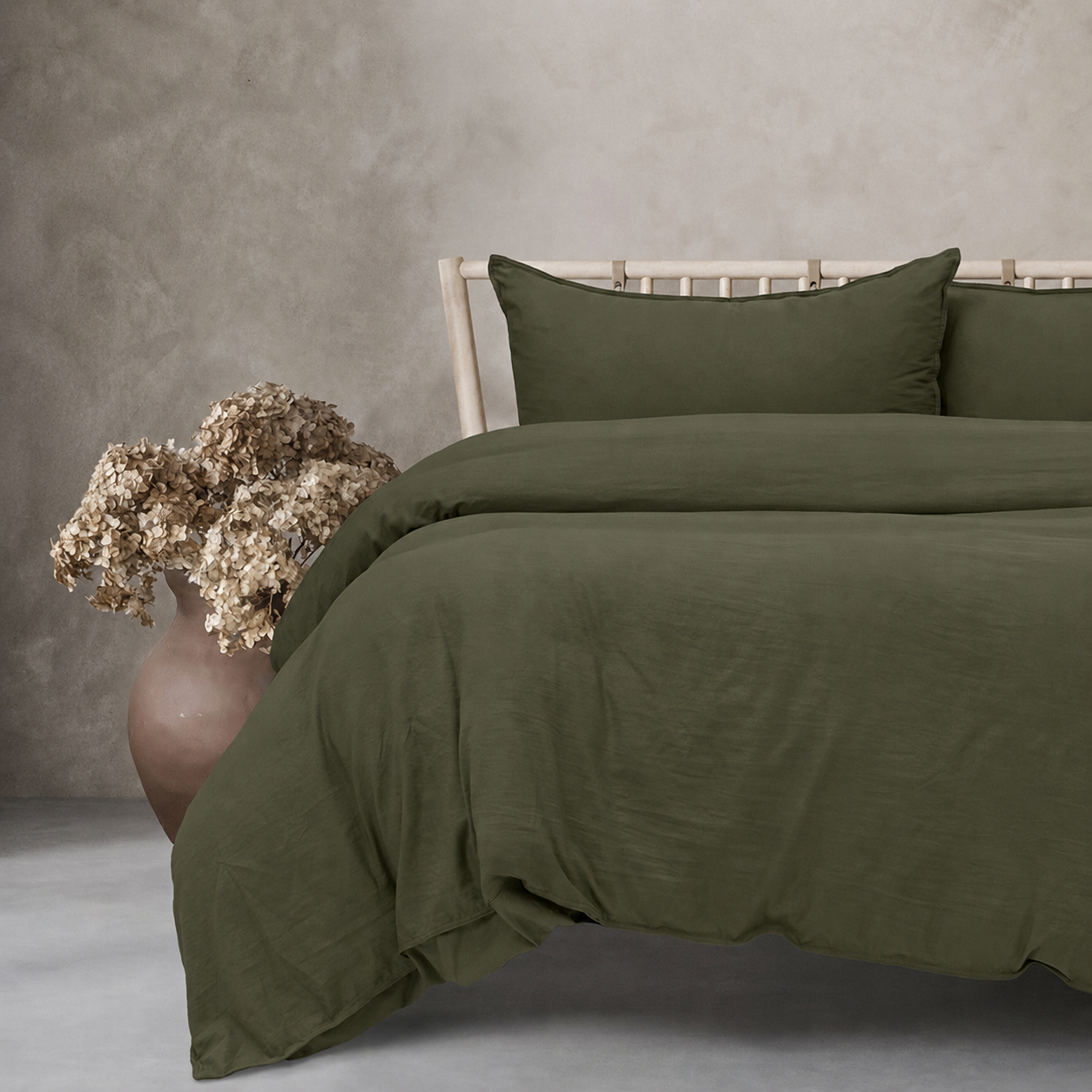 Green bedding set on a bed with a vase of flowers on a gray surface.