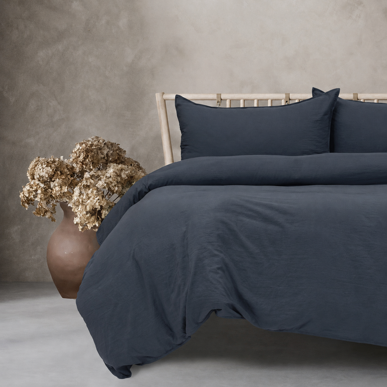 Navy blue bedding set on a bed with a vase of dried flowers on a gray surface.