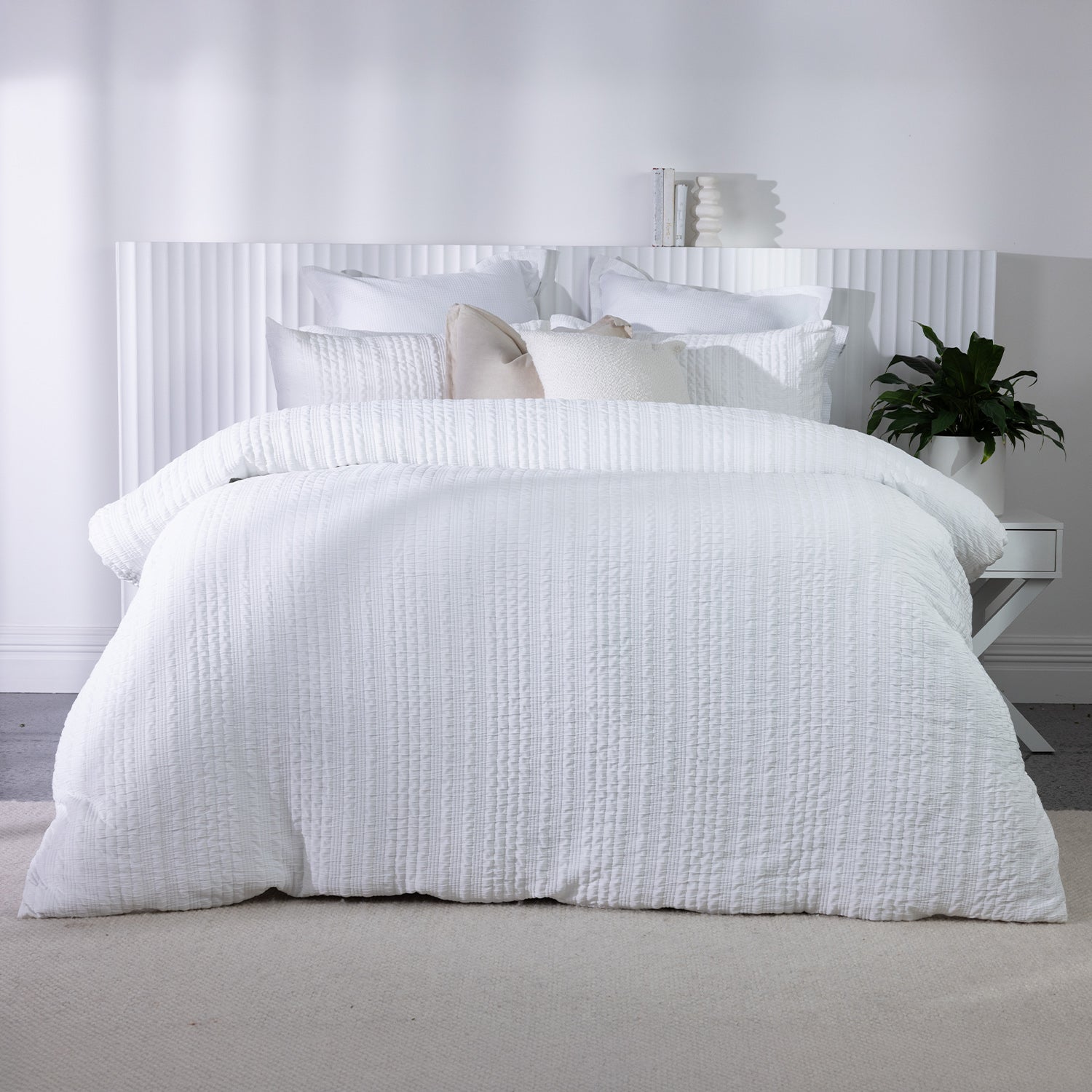 White textured duvet cover set styled on a bed with matching pillowcases and neutral accent cushions in a bright contemporary bedroom.