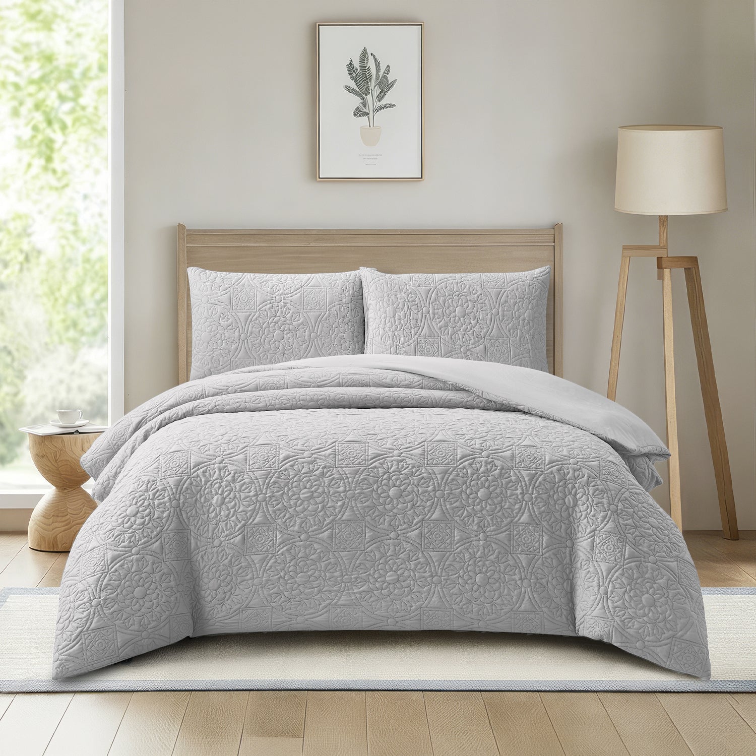 A light gray quilted duvet cover set with matching pillow shams styled on a bed in a bright, modern bedroom with a wooden headboard, floor lamp, and window.