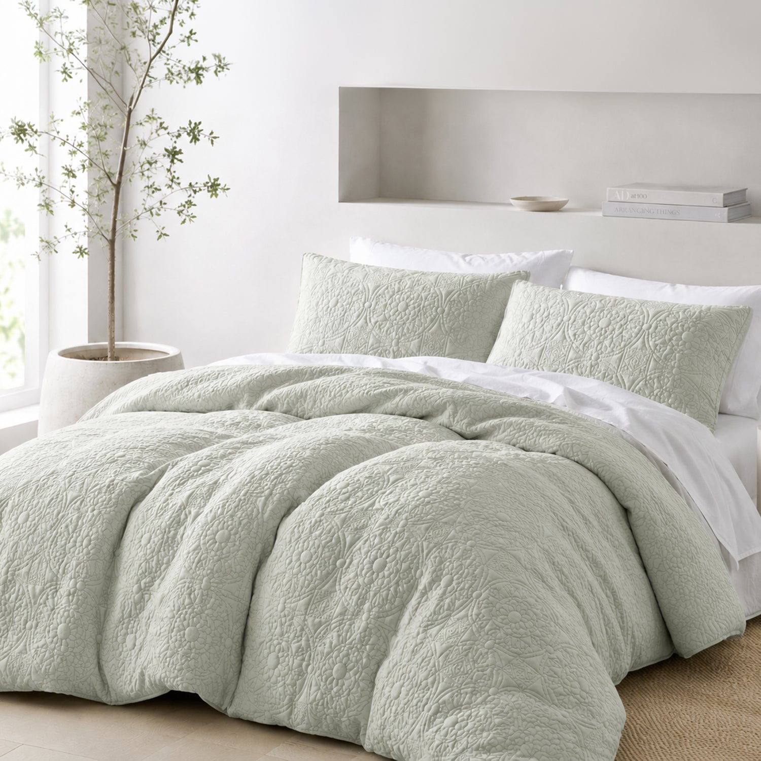 A bed dressed in a textured light sage green bedding set with matching pillow shams and white linens, styled in a bright, modern bedroom with a built-in shelf and a potted tree.