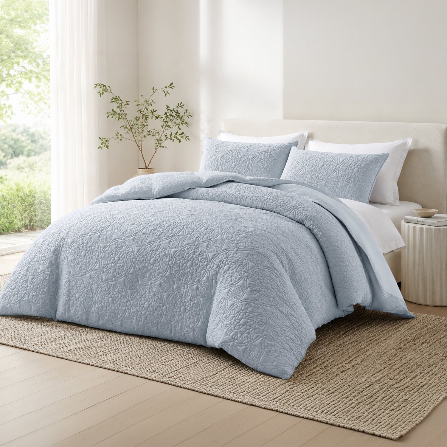 A light blue textured quilted duvet cover set with matching pillow shams on a bed in a bright, modern bedroom with a beige headboard, woven rug, and side table.