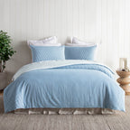 Blue textured bedding set on a bed with white pillows in a bedroom setting.