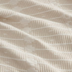 A close-up of a cream-colored quilted fabric with a textured geometric pattern of stitched lines.