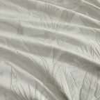 A close-up of textured fabric with a tonal leaf pattern, shown in soft folds with a light gray-green hue.