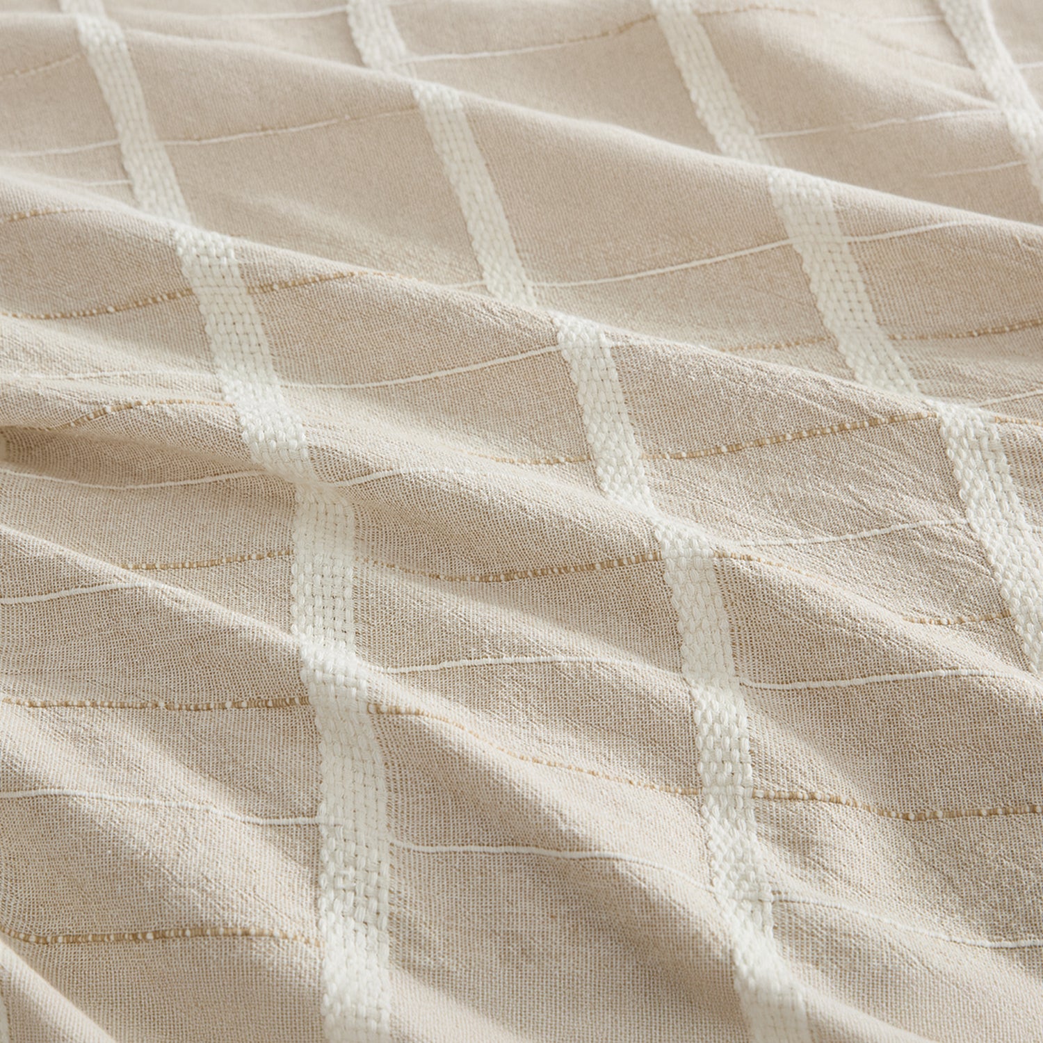 A close-up of a textured fabric with a woven grid pattern in warm beige and off-white.