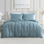 A blue textured duvet cover set, styled on a bed in a bright, modern bedroom with white furniture and a light gray paneled wall.