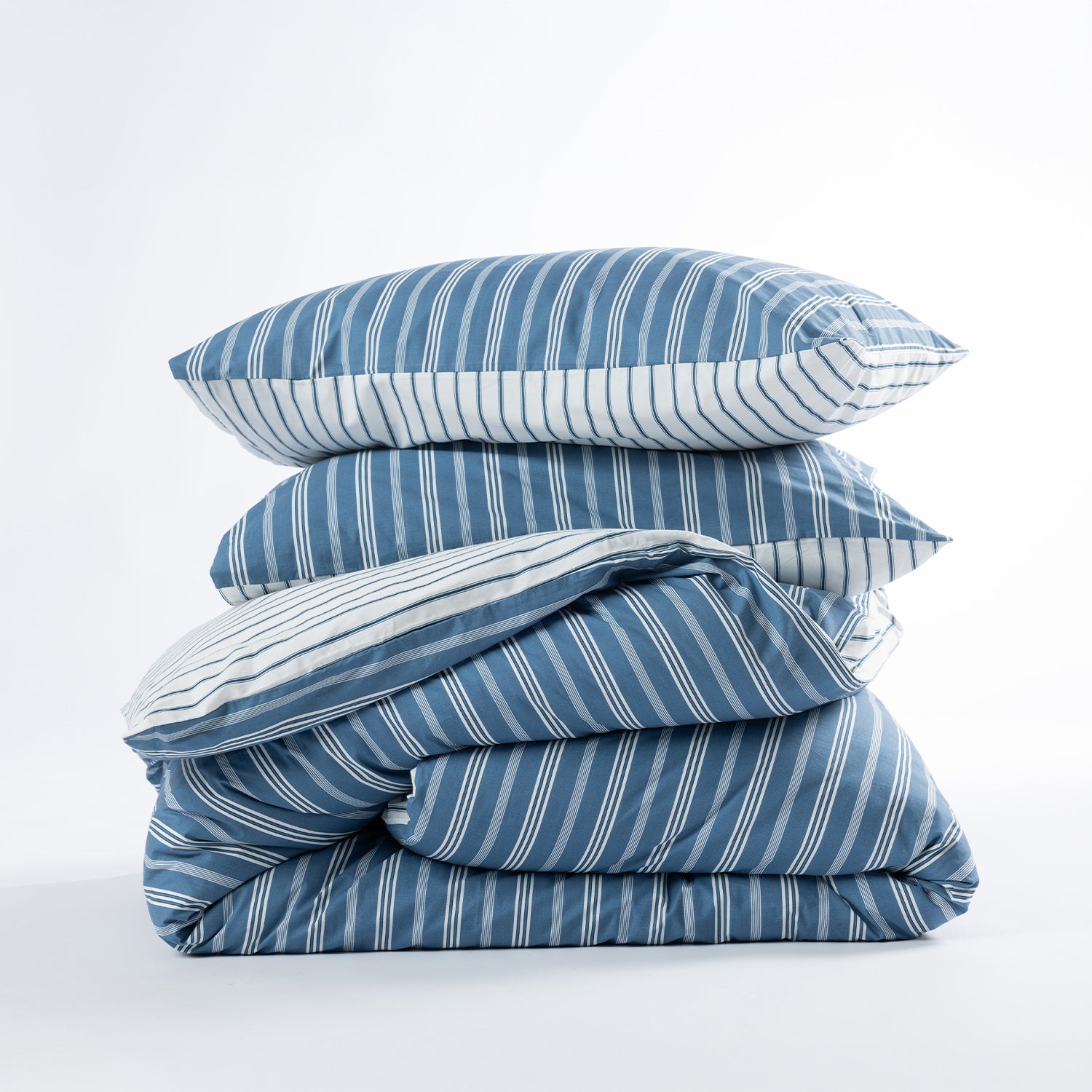A stack of bedding, including two striped pillows and a folded duvet cover, in shades of blue and white with vertical stripes, set against a plain white background.