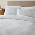 Grey Blue: A bed styled with the Cove Palm Toile Jacquard Duvet Cover Set in grey blue, featuring a delicate palm tree pattern, white trim and matching pillowcases in a softly styled neutral bedroom.