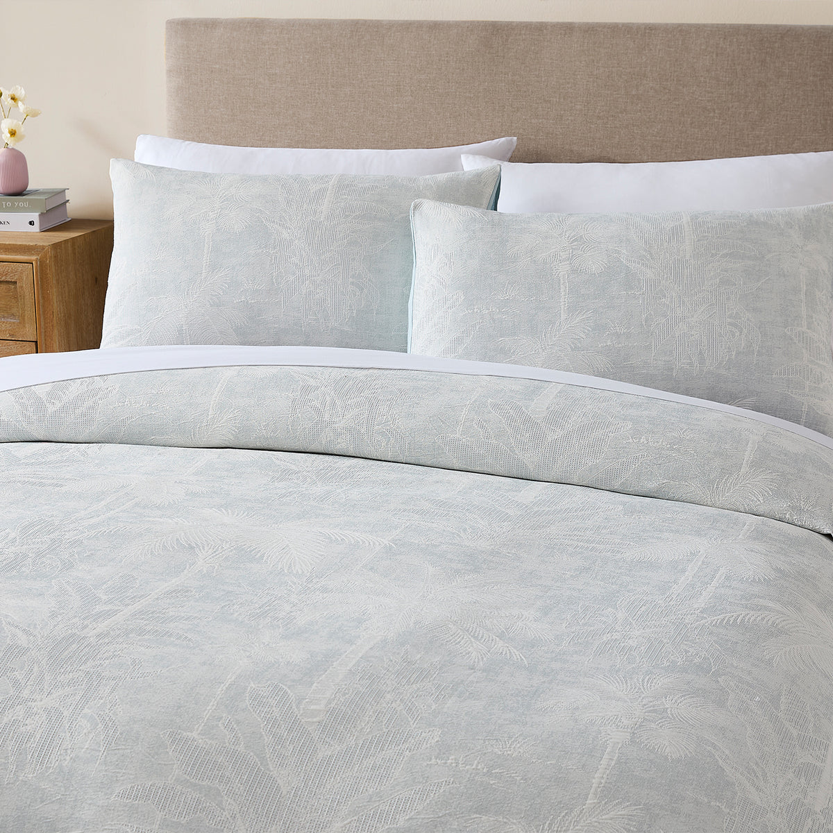 Grey Blue: A bed styled with the Cove Palm Toile Jacquard Duvet Cover Set in grey blue, featuring a delicate palm tree pattern, white trim and matching pillowcases in a softly styled neutral bedroom.