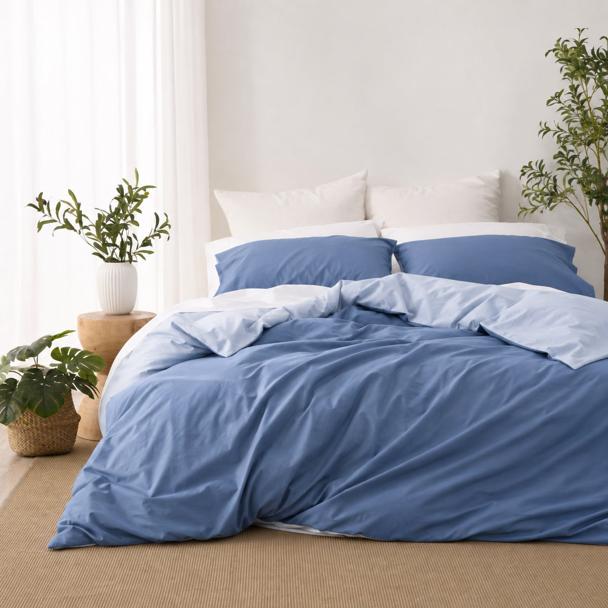 Solace Arden Reversible Duvet Cover Set styled in a blue colourway, featuring a deep blue duvet cover with a lighter blue reverse and coordinating pillowcases in a bright, natural bedroom setting.