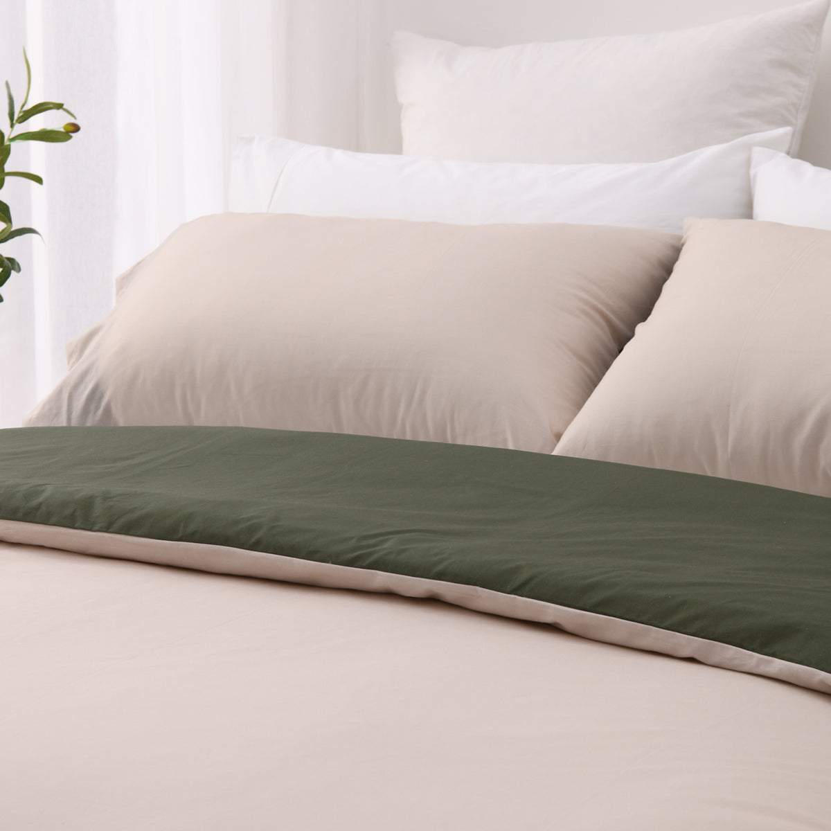 Close-up of the natural side of the Solace Arden Reversible Duvet Cover Set, featuring natural-toned pillowcases with the deep green reverse folded across the bed.