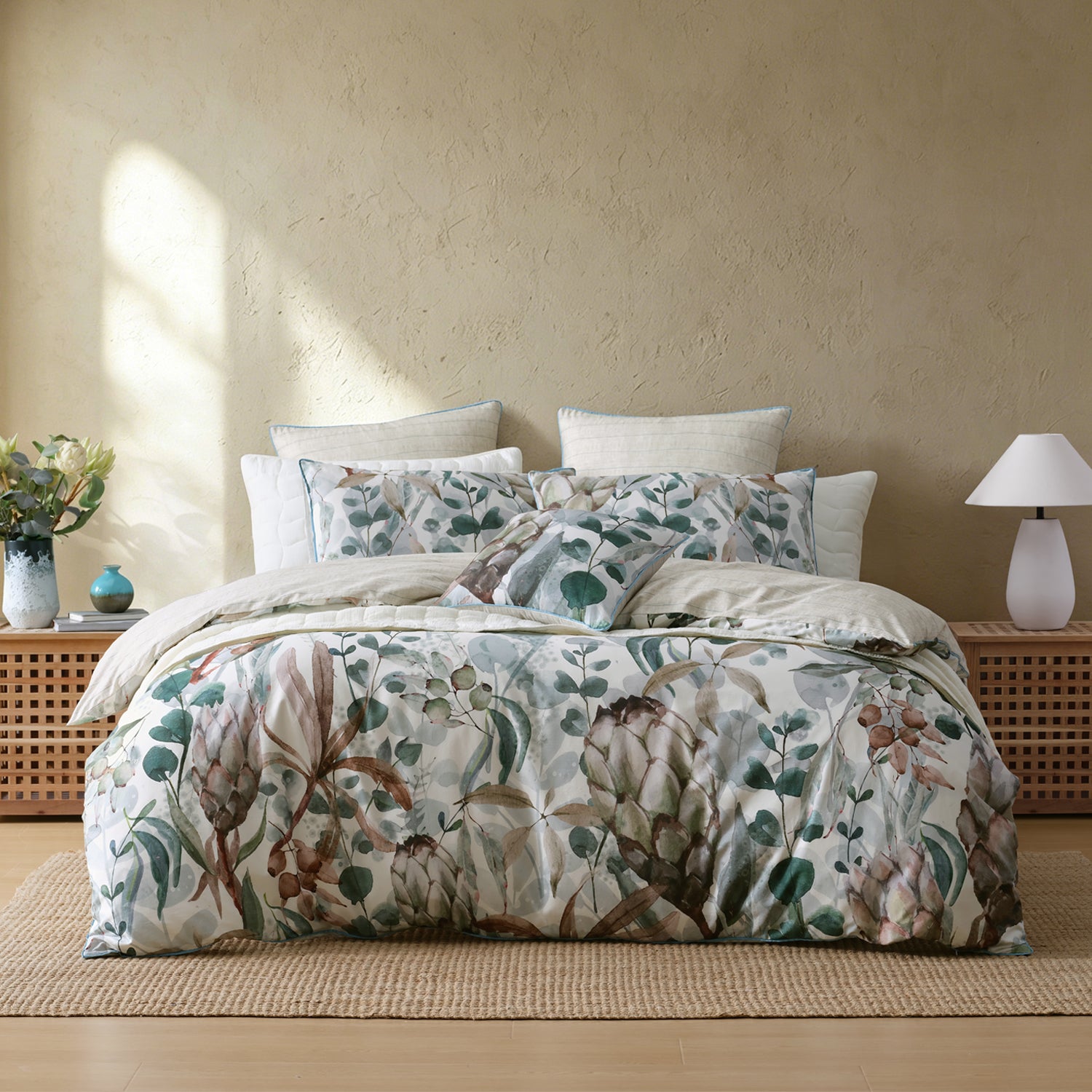 A bed dressed in a botanical print duvet cover and matching pillow shams, styled in a warm, neutral-toned bedroom with wooden bedside tables, a textured wall, and a lamp.
